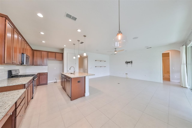 kitchen with open floor plan, appliances with stainless steel finishes, brown cabinetry, and decorative light fixtures