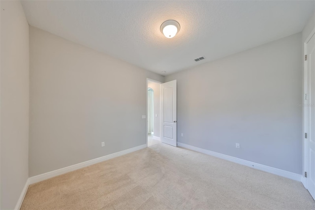 spare room featuring light colored carpet, visible vents, baseboards, and a textured ceiling