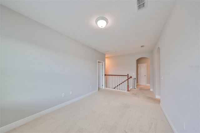 empty room featuring baseboards, visible vents, arched walkways, and light colored carpet