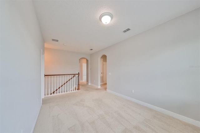 spare room with arched walkways, visible vents, light carpet, and baseboards