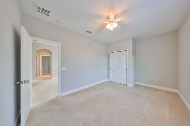 spare room featuring light carpet, visible vents, and arched walkways