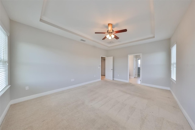 unfurnished bedroom featuring ceiling fan, light carpet, visible vents, baseboards, and a tray ceiling