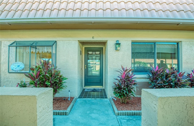 view of exterior entry with a tile roof and stucco siding