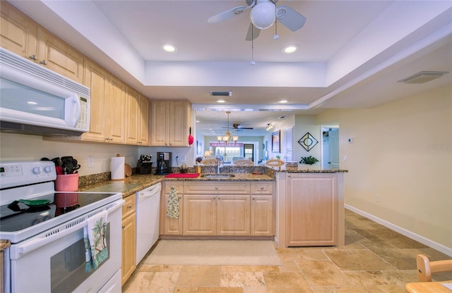 kitchen with a tray ceiling, light brown cabinetry, a sink, white appliances, and a peninsula