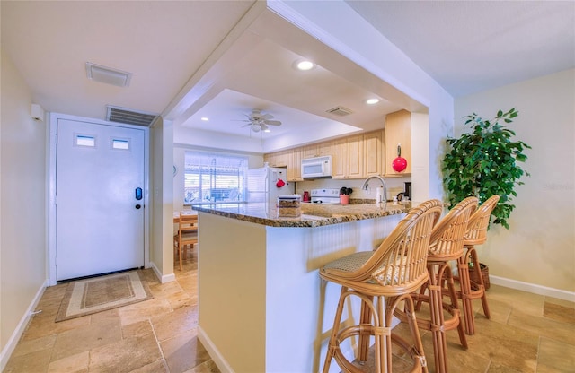 kitchen featuring stone tile floors, visible vents, light brown cabinetry, dark stone countertops, and white appliances