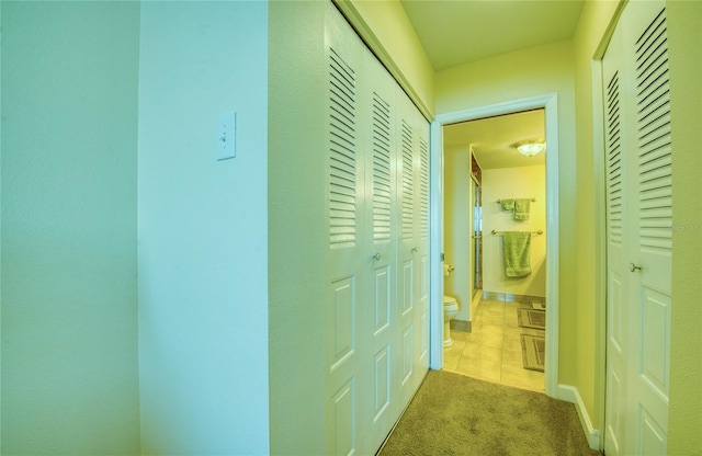 corridor featuring baseboards, carpet flooring, and tile patterned floors