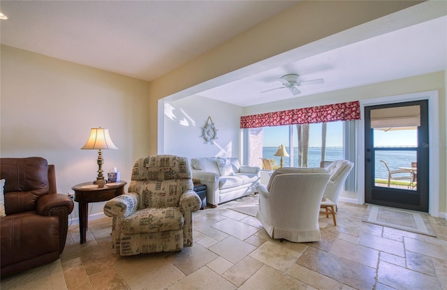 living area featuring a water view, a ceiling fan, baseboards, and stone tile flooring