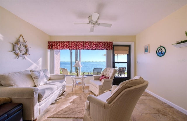 living area with a ceiling fan, stone finish flooring, a water view, and baseboards