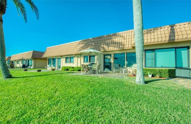 rear view of property with a patio area, a yard, and a tiled roof