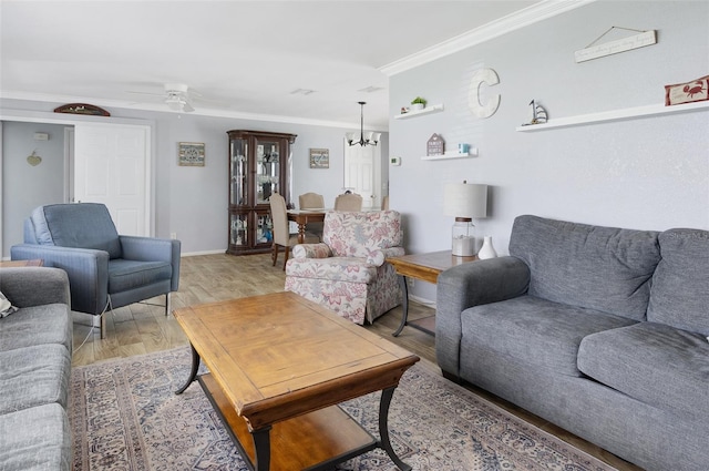 living area featuring light wood-style flooring, ornamental molding, baseboards, and ceiling fan with notable chandelier