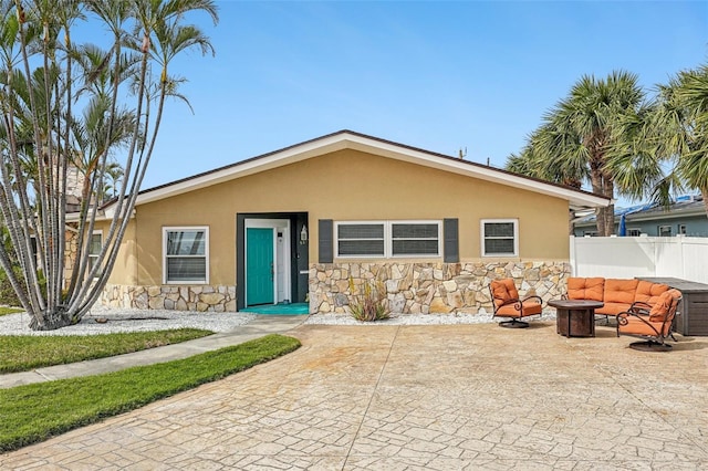 bungalow-style house with stone siding, fence, an outdoor hangout area, a patio, and stucco siding