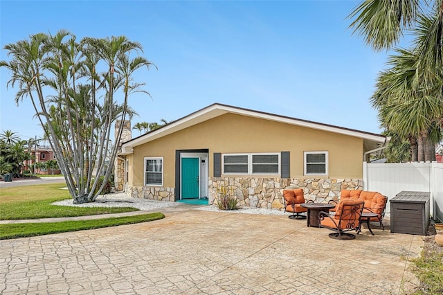 bungalow with stucco siding, stone siding, fence, and a patio area