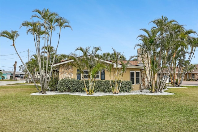 view of front of property featuring stone siding, a chimney, a front yard, and stucco siding