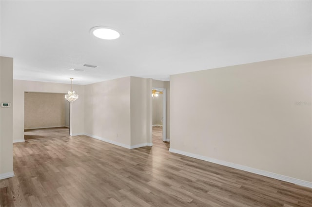 unfurnished room featuring a notable chandelier, baseboards, and wood finished floors