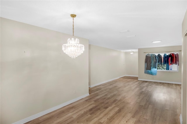 empty room featuring a notable chandelier, baseboards, and wood finished floors