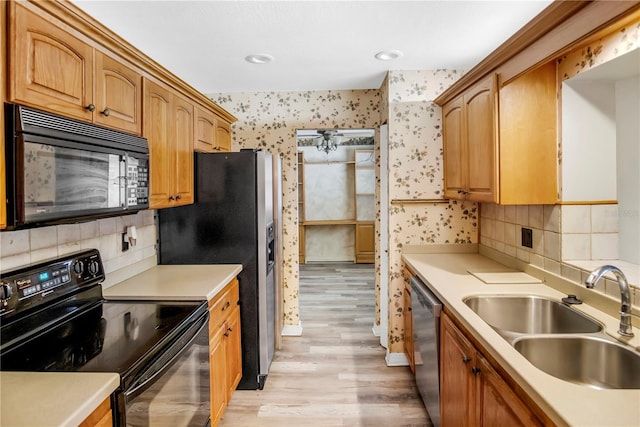 kitchen with wallpapered walls, light wood-style flooring, light countertops, black appliances, and a sink