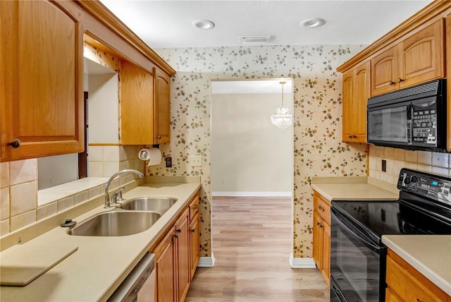 kitchen with black appliances, wallpapered walls, light countertops, and a sink