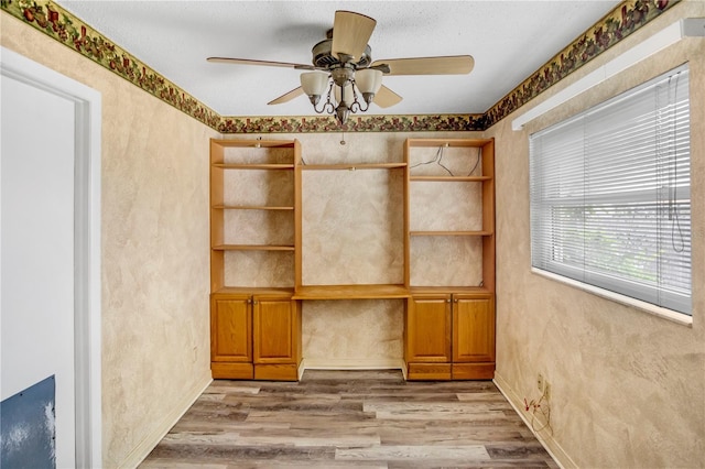 empty room featuring a ceiling fan, wood finished floors, and built in study area