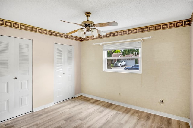 unfurnished bedroom featuring light wood finished floors, baseboards, a ceiling fan, a textured ceiling, and two closets