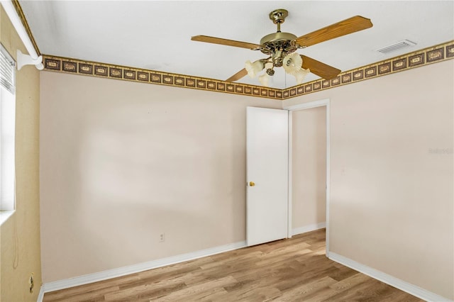 spare room featuring a ceiling fan, visible vents, baseboards, and wood finished floors