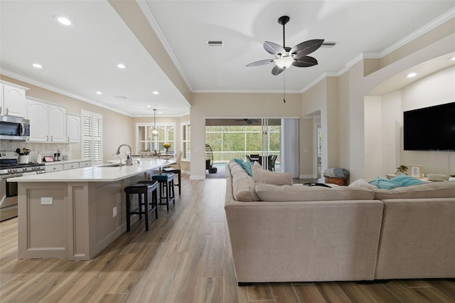 living room featuring a ceiling fan, visible vents, light wood finished floors, and ornamental molding