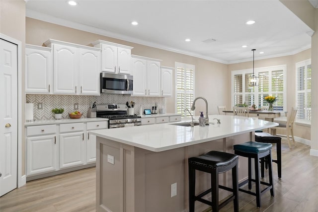 kitchen featuring ornamental molding, decorative backsplash, a sink, appliances with stainless steel finishes, and a kitchen breakfast bar