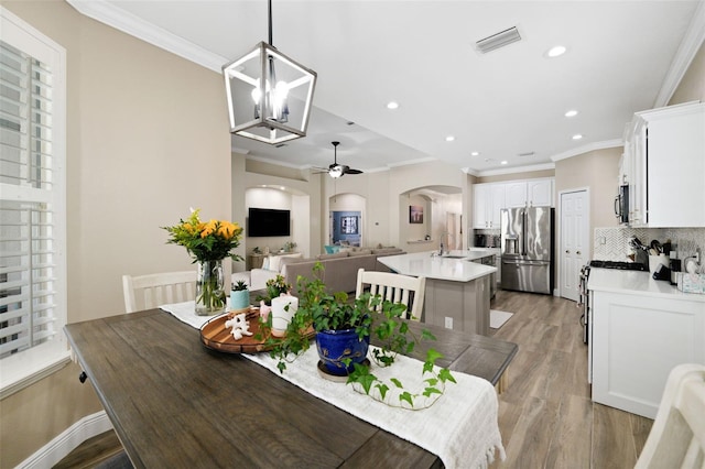 dining room with visible vents, light wood-type flooring, ornamental molding, recessed lighting, and arched walkways