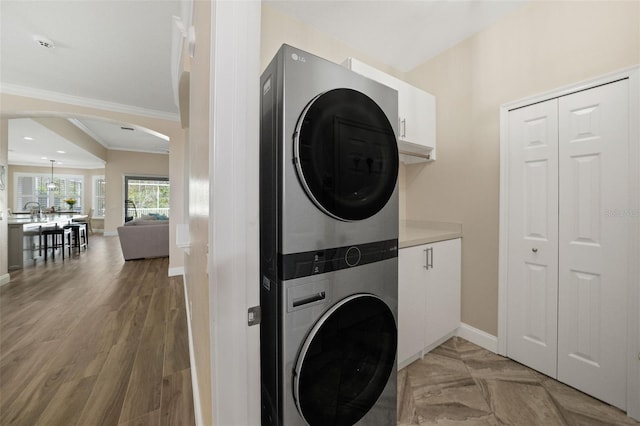 laundry room featuring crown molding, baseboards, arched walkways, cabinet space, and stacked washer / drying machine