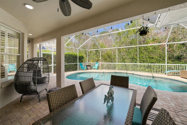 view of swimming pool with a fenced in pool, glass enclosure, a patio area, outdoor dining space, and a ceiling fan