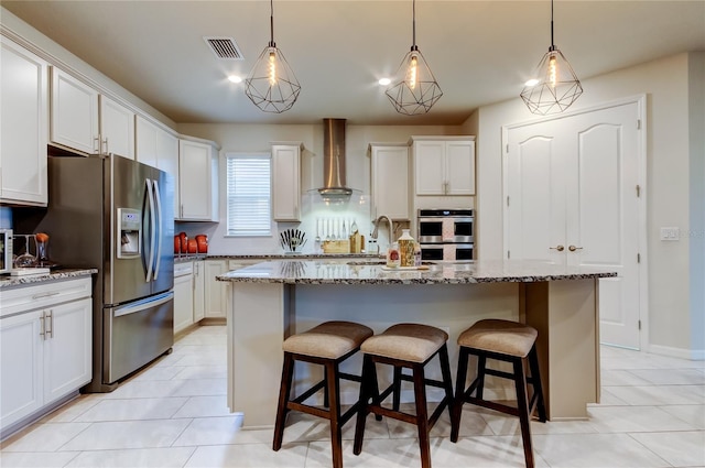 kitchen featuring a kitchen bar, white cabinets, appliances with stainless steel finishes, and wall chimney exhaust hood