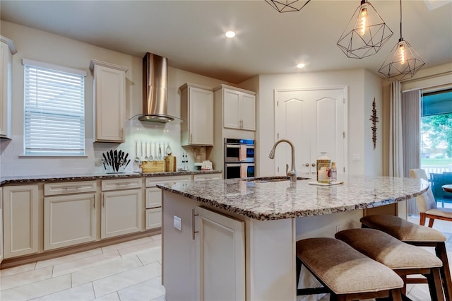 kitchen with a sink, a kitchen breakfast bar, tasteful backsplash, wall chimney range hood, and light stone countertops