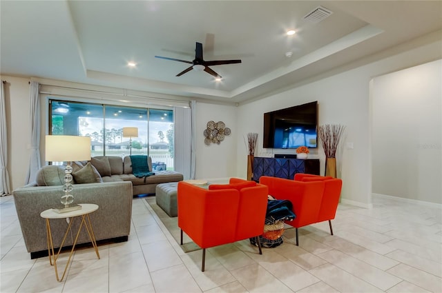 living area featuring light tile patterned floors, a ceiling fan, baseboards, visible vents, and a raised ceiling