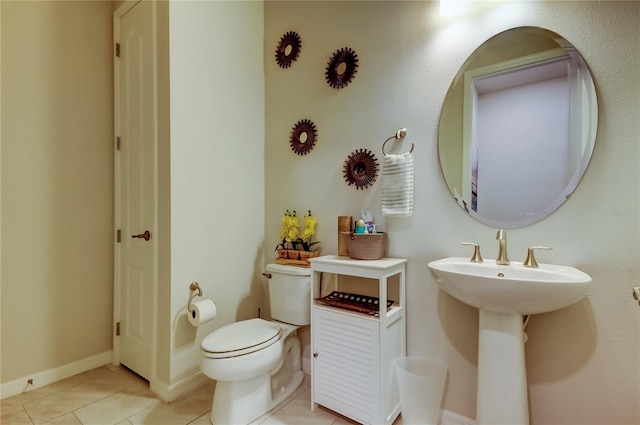 half bathroom featuring tile patterned flooring, toilet, baseboards, and a sink