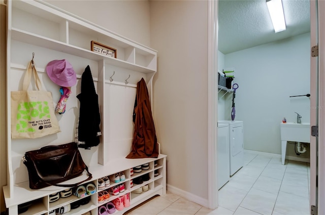 mudroom featuring washer and clothes dryer, light tile patterned floors, a textured ceiling, and baseboards