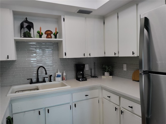 kitchen featuring light countertops, a sink, freestanding refrigerator, and white cabinetry