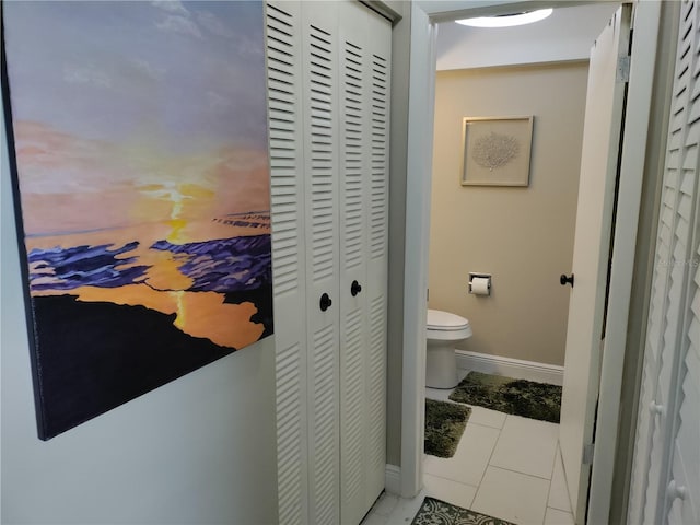 bathroom featuring toilet, tile patterned flooring, baseboards, and a closet