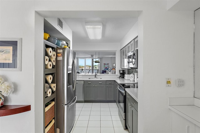 kitchen featuring light tile patterned floors, light countertops, gray cabinetry, appliances with stainless steel finishes, and a sink