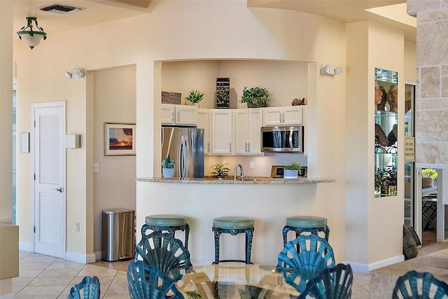 kitchen with visible vents, white cabinets, appliances with stainless steel finishes, light stone countertops, and light tile patterned flooring