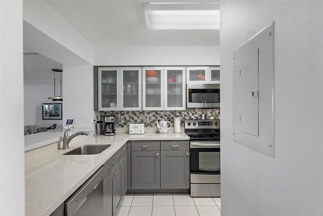 kitchen featuring light tile patterned floors, gray cabinetry, a sink, appliances with stainless steel finishes, and decorative backsplash