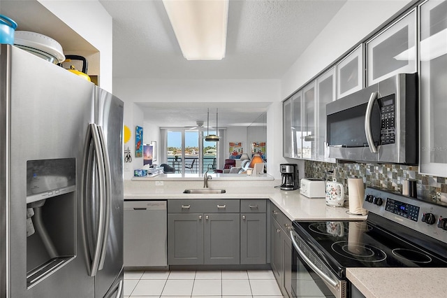 kitchen featuring glass insert cabinets, appliances with stainless steel finishes, light countertops, gray cabinetry, and a sink