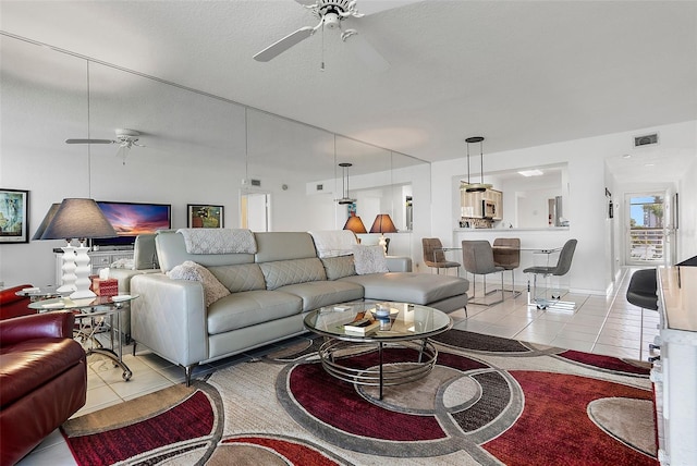 living area featuring light tile patterned floors, a textured ceiling, visible vents, and a ceiling fan