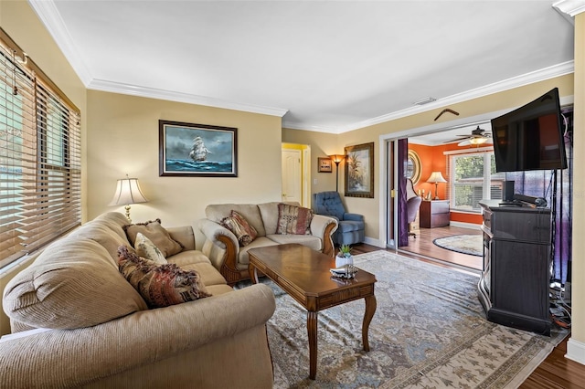 living room with wood finished floors, visible vents, a ceiling fan, baseboards, and ornamental molding