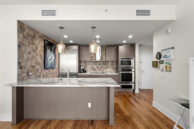 kitchen featuring pendant lighting, visible vents, appliances with stainless steel finishes, wall chimney range hood, and a peninsula