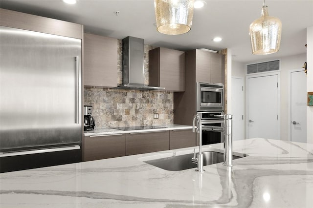 kitchen with light stone counters, stainless steel appliances, a sink, wall chimney range hood, and modern cabinets