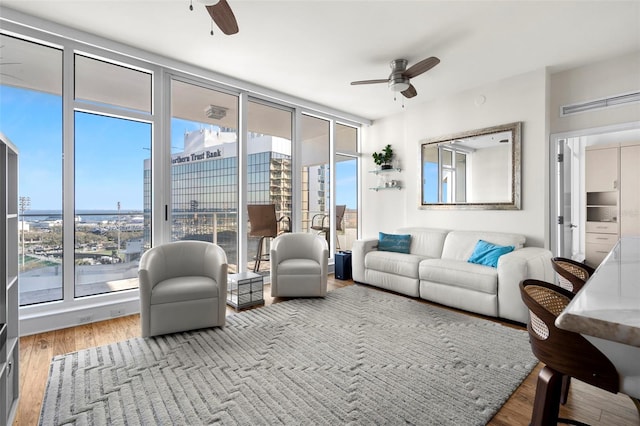 living area featuring expansive windows, ceiling fan, a view of city, and wood finished floors