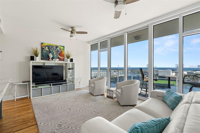 living room with expansive windows, ceiling fan, wood finished floors, and baseboards