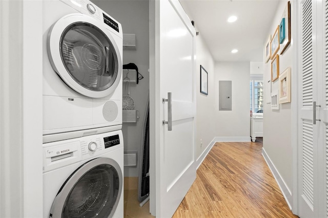 laundry area with laundry area, electric panel, baseboards, stacked washer / drying machine, and light wood-type flooring