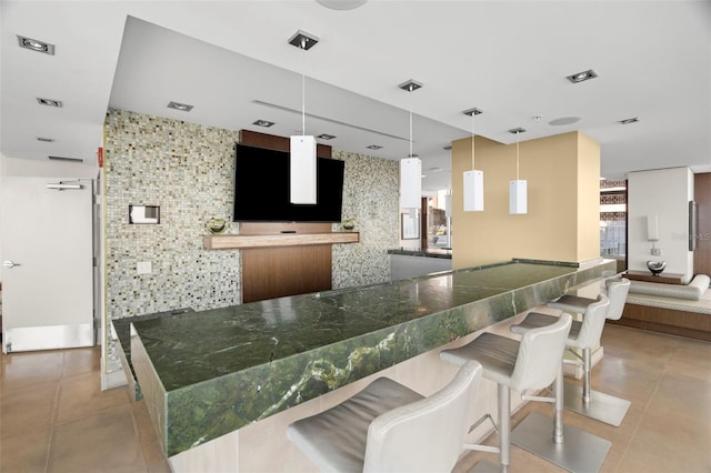 kitchen featuring dark countertops, light tile patterned flooring, decorative light fixtures, and a breakfast bar area