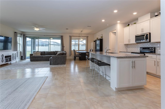 kitchen featuring stainless steel appliances, a sink, white cabinetry, open floor plan, and an island with sink