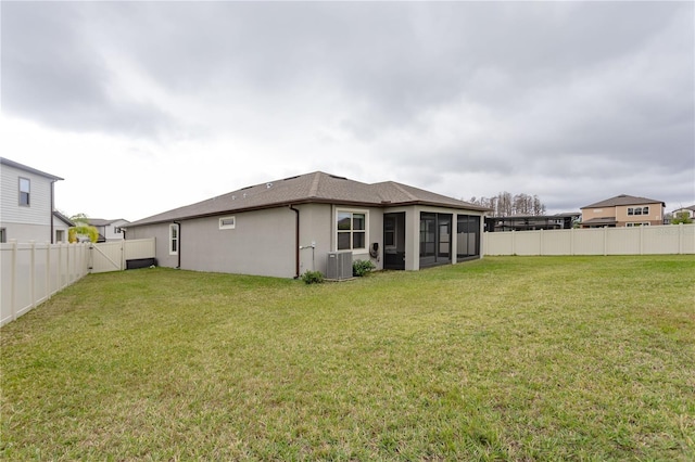 rear view of property featuring a sunroom, a fenced backyard, a yard, central AC, and stucco siding